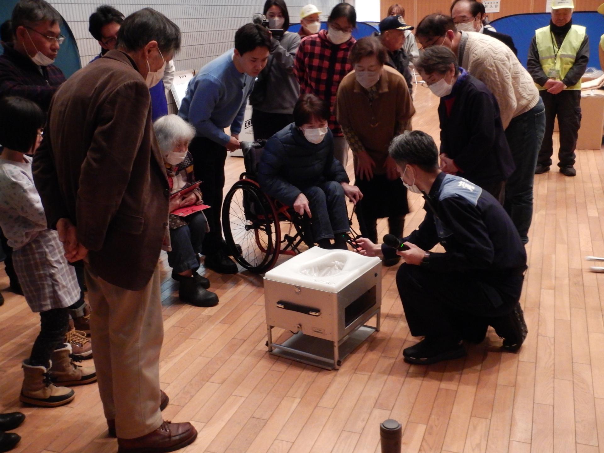 自動ラップ式トイレの実演を見学する参加者
