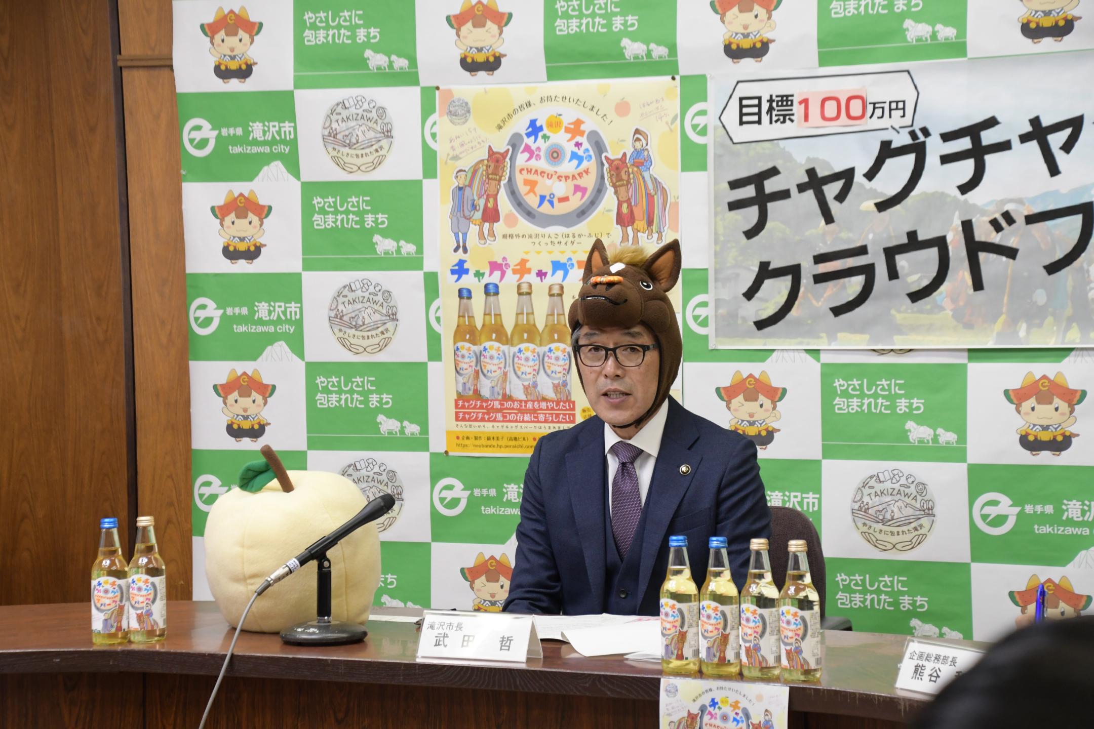 馬の被り物を被り記者へ説明する滝沢市長