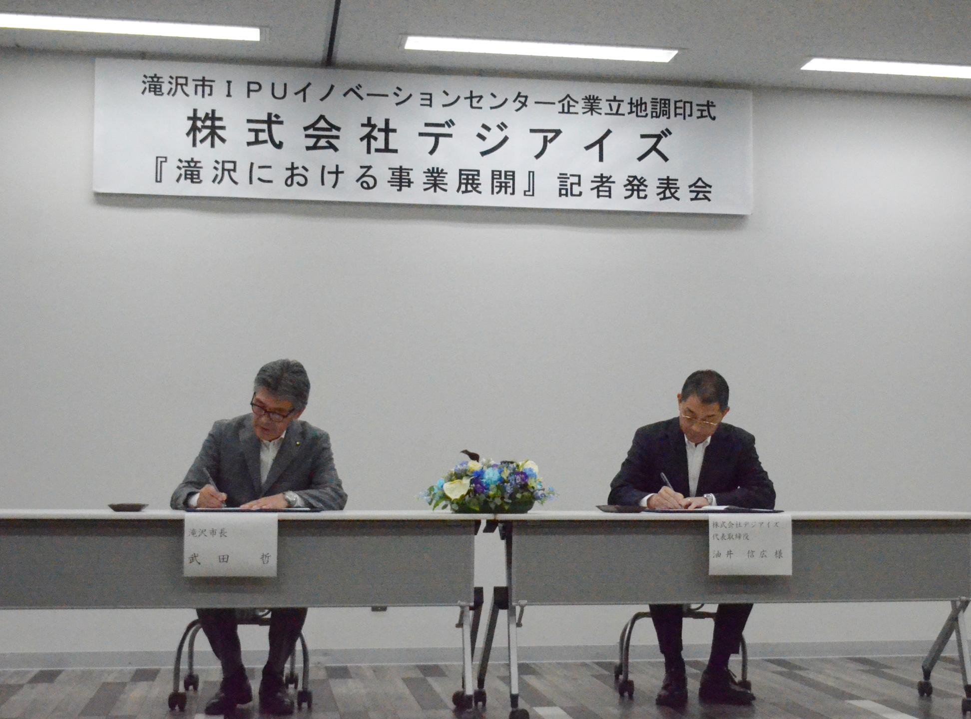 協定書に署名する油井代表取締役と武田市長