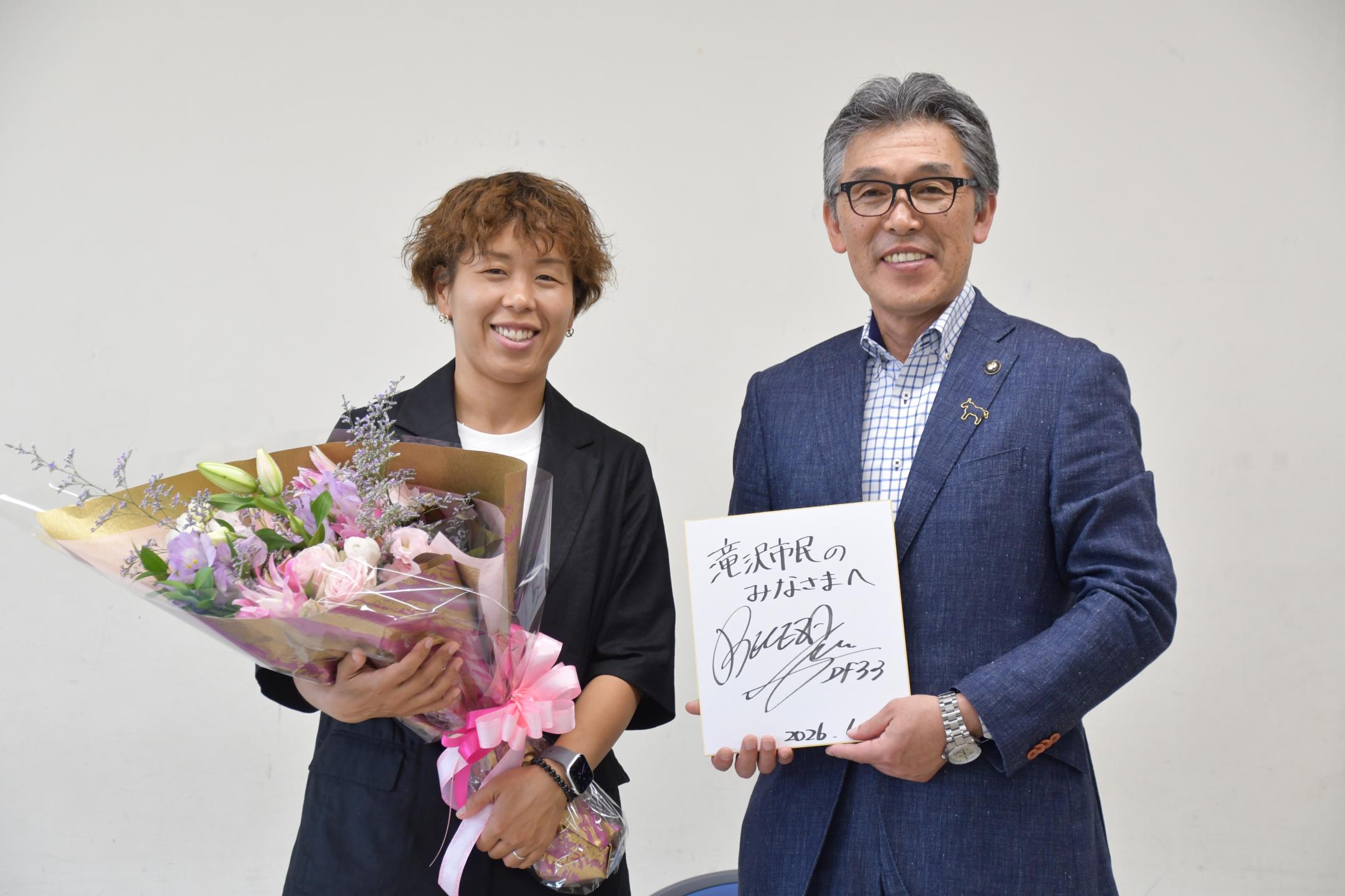 花束を手にする岩清水さんとサインを手にする市長
