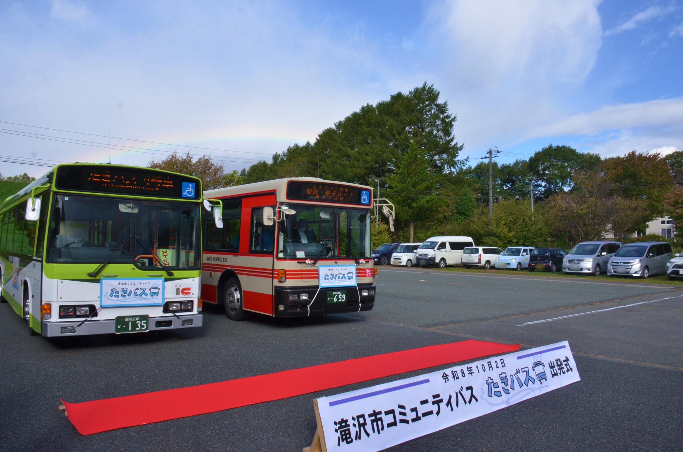 たきバス車両が並び、空に虹がかかっている様子