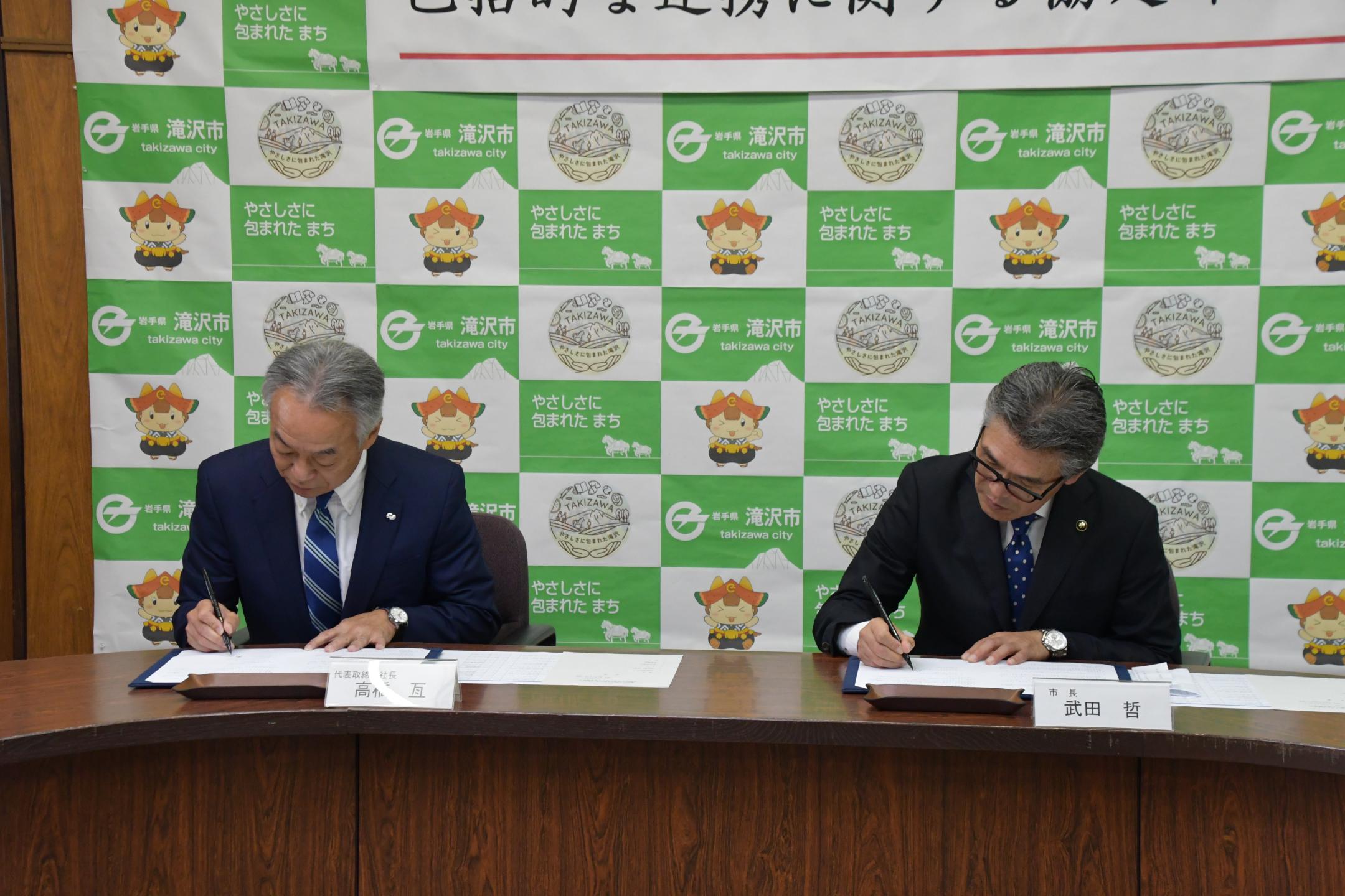 協定書に記名している武田市長と高橋代表取締役社長